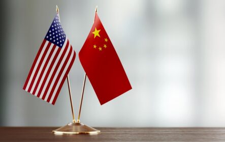 American And Chinese Flag Pair On A Desk Over Defocused Background
